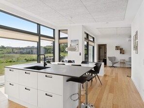 Eine moderne Küche mit einer großen Kochinsel, Barhocker und Blick ins Freie.