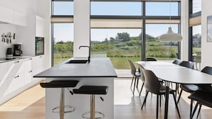 A modern kitchen with a central island, large windows, and a dining area with chairs. - 4 Star Holiday Home in Allinge (Allinge)