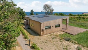 A modern wooden cabin with a flat roof, a deck, and a view of the sea. - 4 Star Holiday Home in Allinge (Allinge)