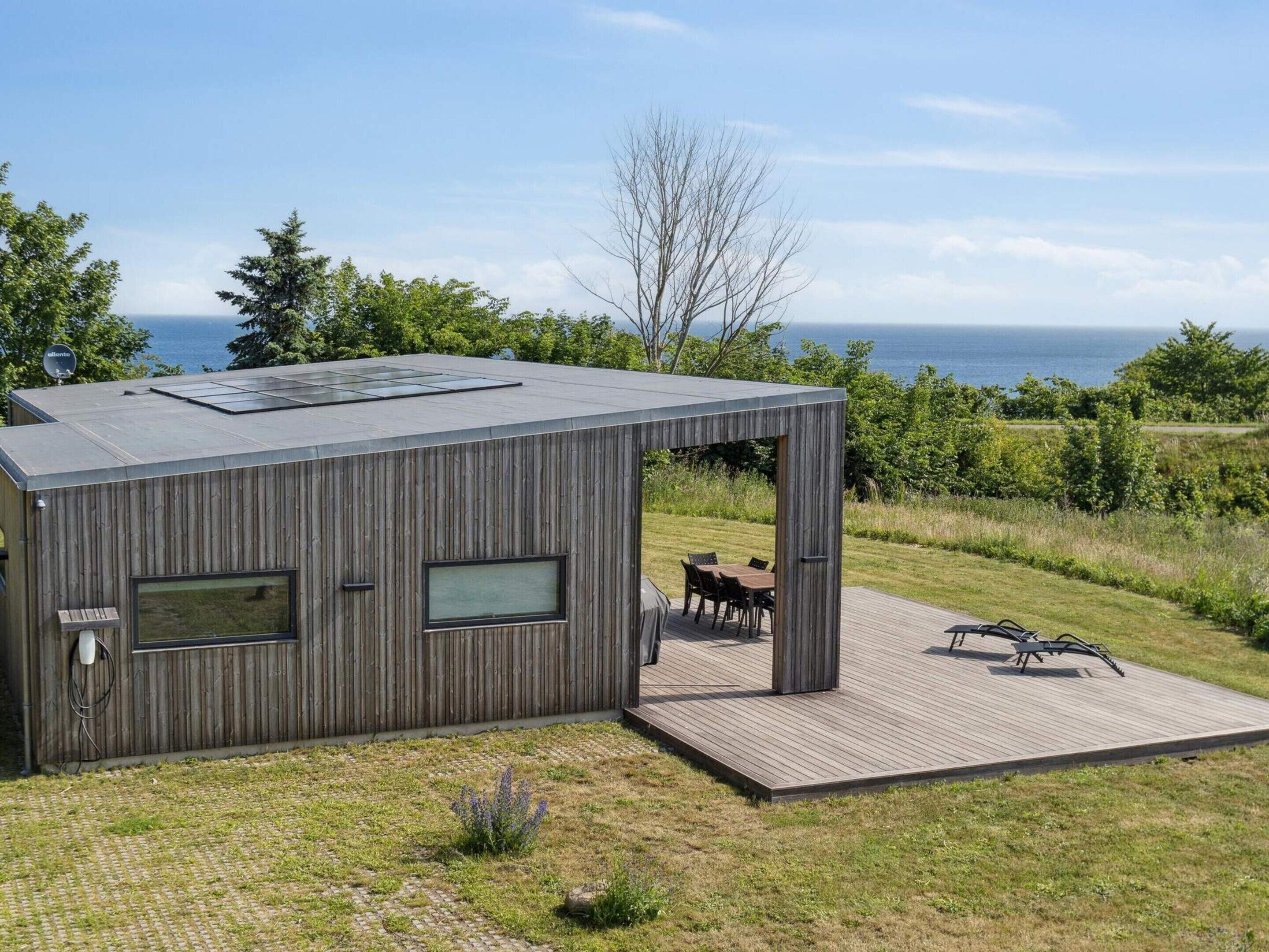 Eine moderne Holz-Blockhütte mit einer Terrasse, großen Fenstern und Meerblick.