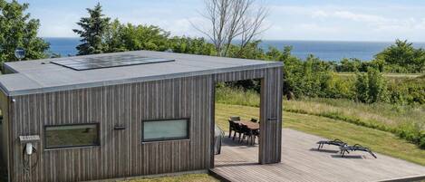 Eine moderne Holz-Blockhütte mit einer Terrasse, großen Fenstern und Meerblick.