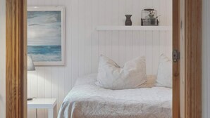 A bedroom with a bed, pillows, a nightstand, a lamp, a framed painting, and a shelf with decorative items. - 4 Star Holiday Home in Borup (Borup)