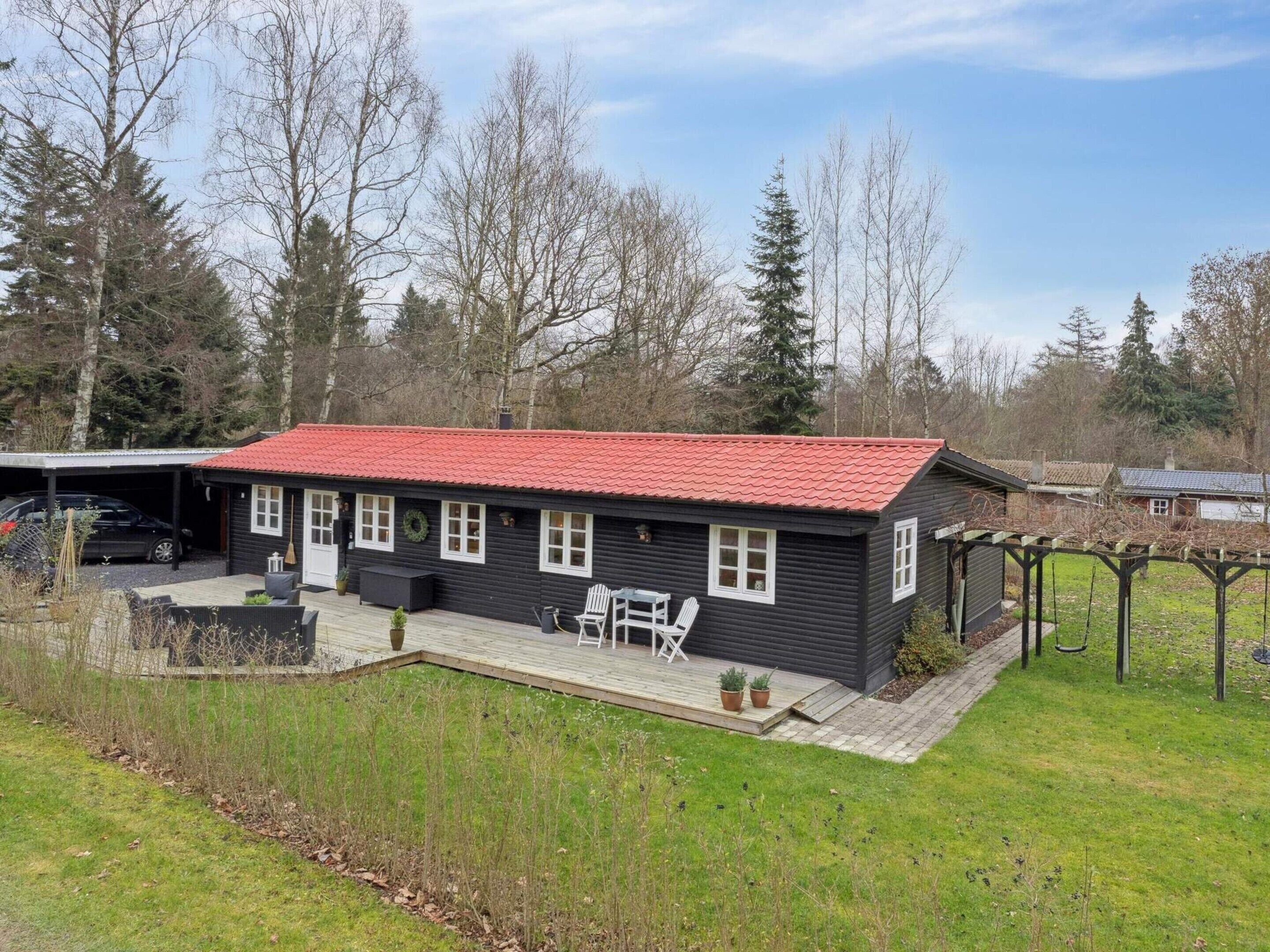 A black wooden house with a red roof, a covered porch with outdoor furniture, and a garden area.