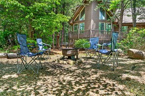 Une cabane dotée d’une terrasse, entourée d’arbres, et aménagée avec un espace salon extérieur et un foyer.