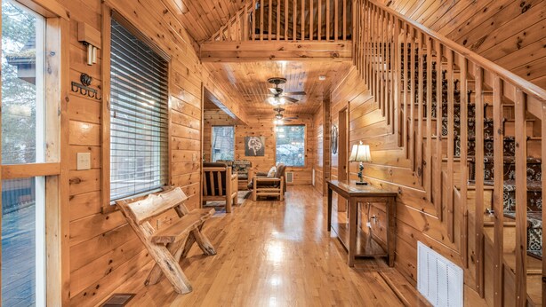 A wooden cabin interior with a staircase, wooden walls, a bench, a table, and a window. - Bear Alley 4 Bedroom Cabin (Gatlinburg)