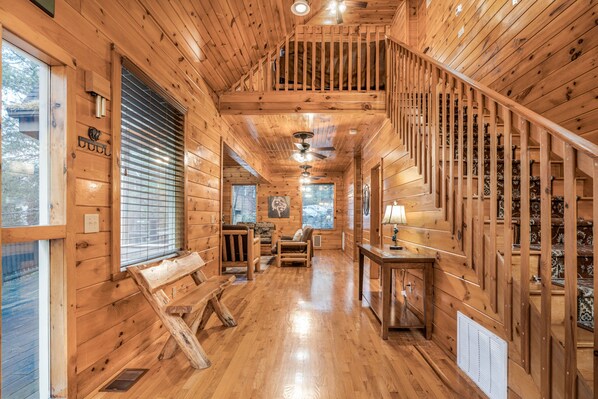 L’intérieur d’un chalet en bois, avec un escalier, des murs en bois, un banc, une table et une fenêtre.