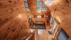 A wooden cabin interior with a dining area, staircase, and multiple windows. - Bear Alley 4 Bedroom Cabin (Gatlinburg)