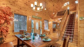 A wooden interior with a dining table set, a staircase, and a sign reading 'FAITH- HOPE- LOVE'. - Bear Alley 4 Bedroom Cabin (Gatlinburg)