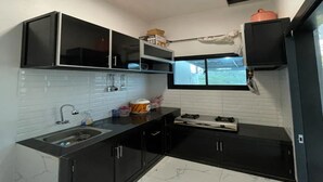 A compact kitchen with black cabinets, a white tiled backsplash, a sink, a window, and a stove. - cozzy Salabim Villa Pangalengan (bandung)