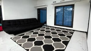 A living room with a black sofa, a patterned rug, a white ceiling, and a window with a view. - cozzy Salabim Villa Pangalengan (bandung)