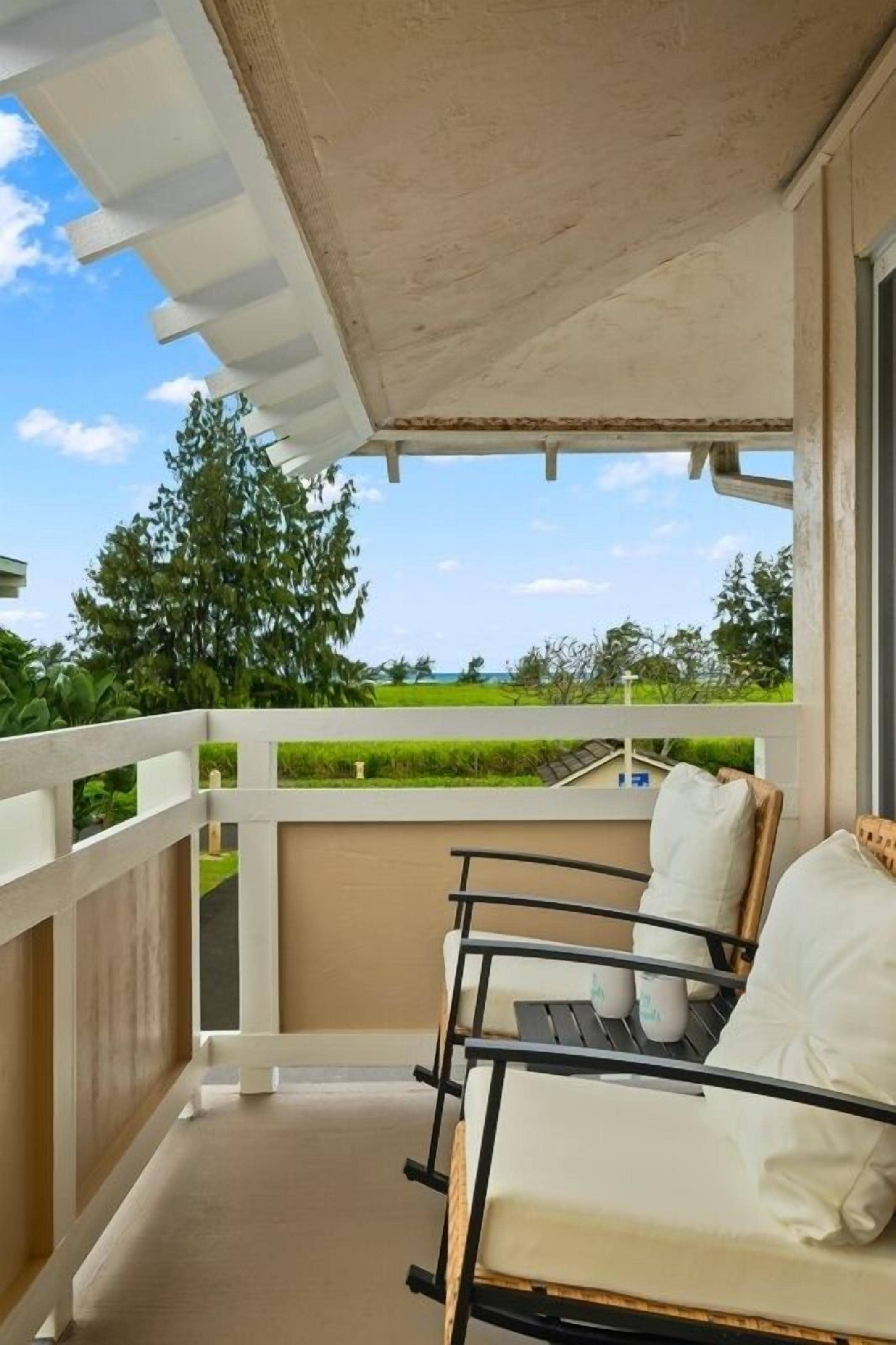 A balcony with a white railing, a cushioned chair, and a view of greenery.