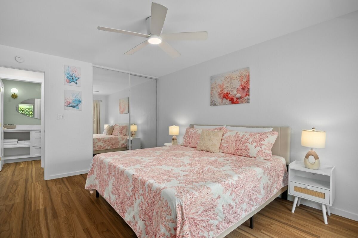 A bedroom with a bed, bedside tables, a ceiling fan, and artwork on the walls.