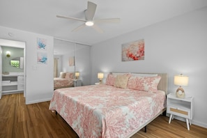 A bedroom with a bed, bedside tables, a ceiling fan, and artwork on the walls. - Kauai Plantation Hale Suites H16 1 Bedroom Condo (Kapaa)