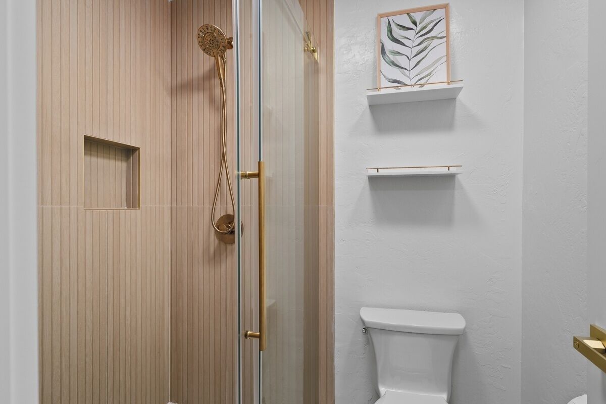 Een badkamer met een douche, toilet en planken met kunstwerken in lijsten.