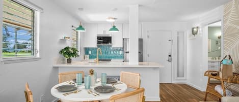 A modern kitchen with white cabinets, a central island, and a dining area with a round table and wicker chairs.