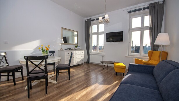 A modern living room with a sofa, chairs, a dining table, and a TV. - InPoint Boutique Apartments near MainSQ (Kraków)