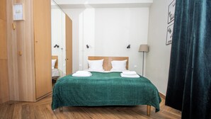 A neatly made bed with a green checkered bedspread, wooden flooring, a wooden wardrobe, a mirror, and a dark curtain. - InPoint Boutique Apartments near MainSQ (Kraków)