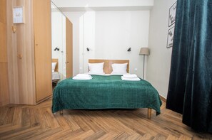 A neatly made bed with a green checkered bedspread, wooden flooring, a wooden wardrobe, a mirror, and a dark curtain. - InPoint Boutique Apartments near MainSQ (Kraków)
