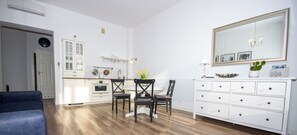 A modern kitchen with white cabinetry, a dining area with two chairs, a white dresser, and a large mirror. - InPoint Boutique Apartments near MainSQ (Kraków)