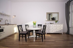 A modern kitchen with white cabinetry, a round dining table with chairs, a white dresser, and a mirror above the dresser. - InPoint Boutique Apartments near MainSQ (Kraków)