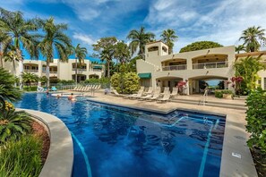 A swimming pool with lounge chairs and palm trees, surrounded by multi-story buildings with balconies. - Palms At Wailea 301 1 Bedroom Condo (Kihei)
