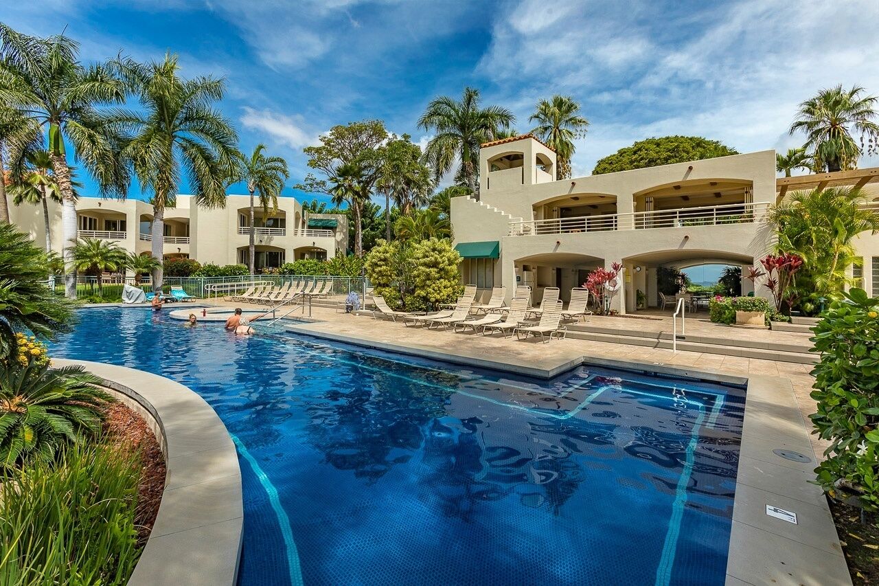 Un hotel con piscina, palmeras y un edificio de varios pisos con balcones.