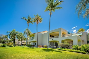 Un hotel moderno con una estructura de dos pisos, con balcones y un césped bien cuidado con palmeras.