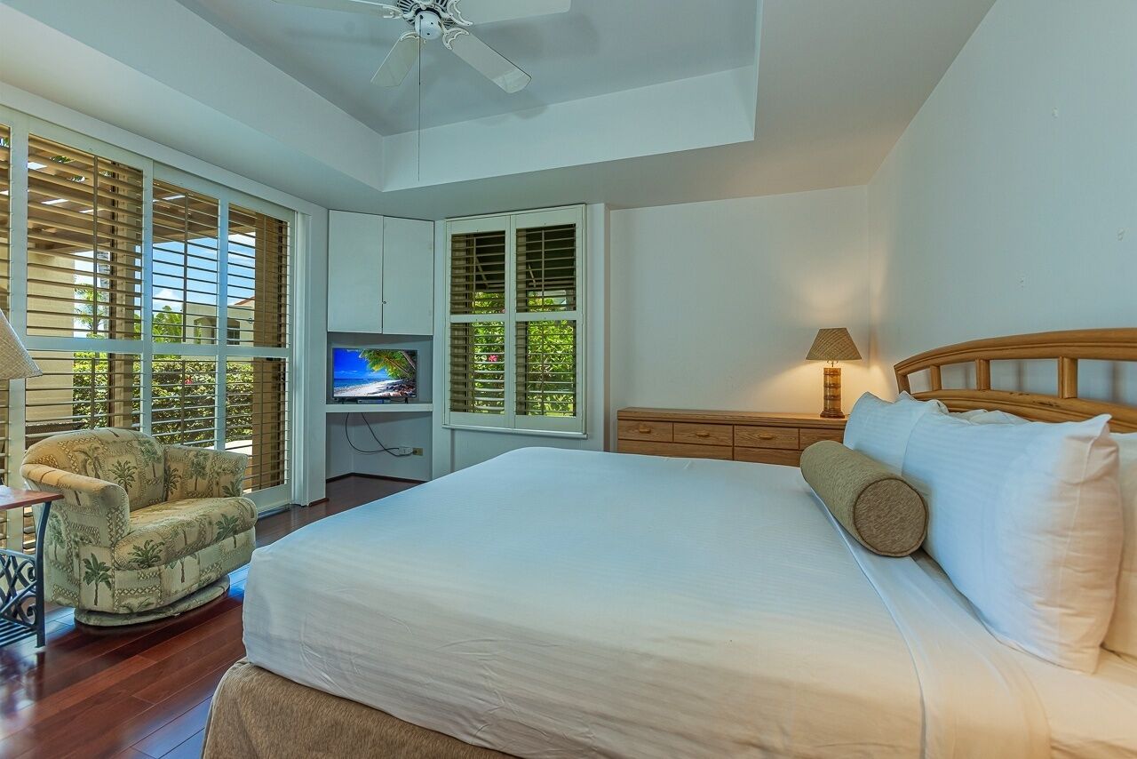 A bedroom with a bed, a television, a chair, and a ceiling fan.