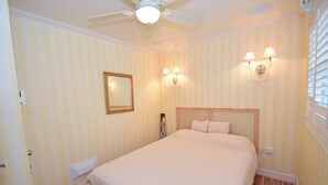 Ein Schlafzimmer mit einem Bett, einem Deckenventilator, einem Spiegel und Wandleuchten.