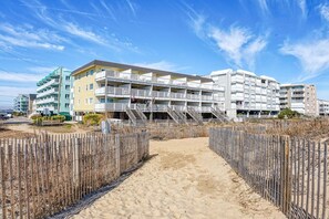 Ein Hotel am Strand mit mehreren Balkonen, einem Sandweg und einem Holzzaun.