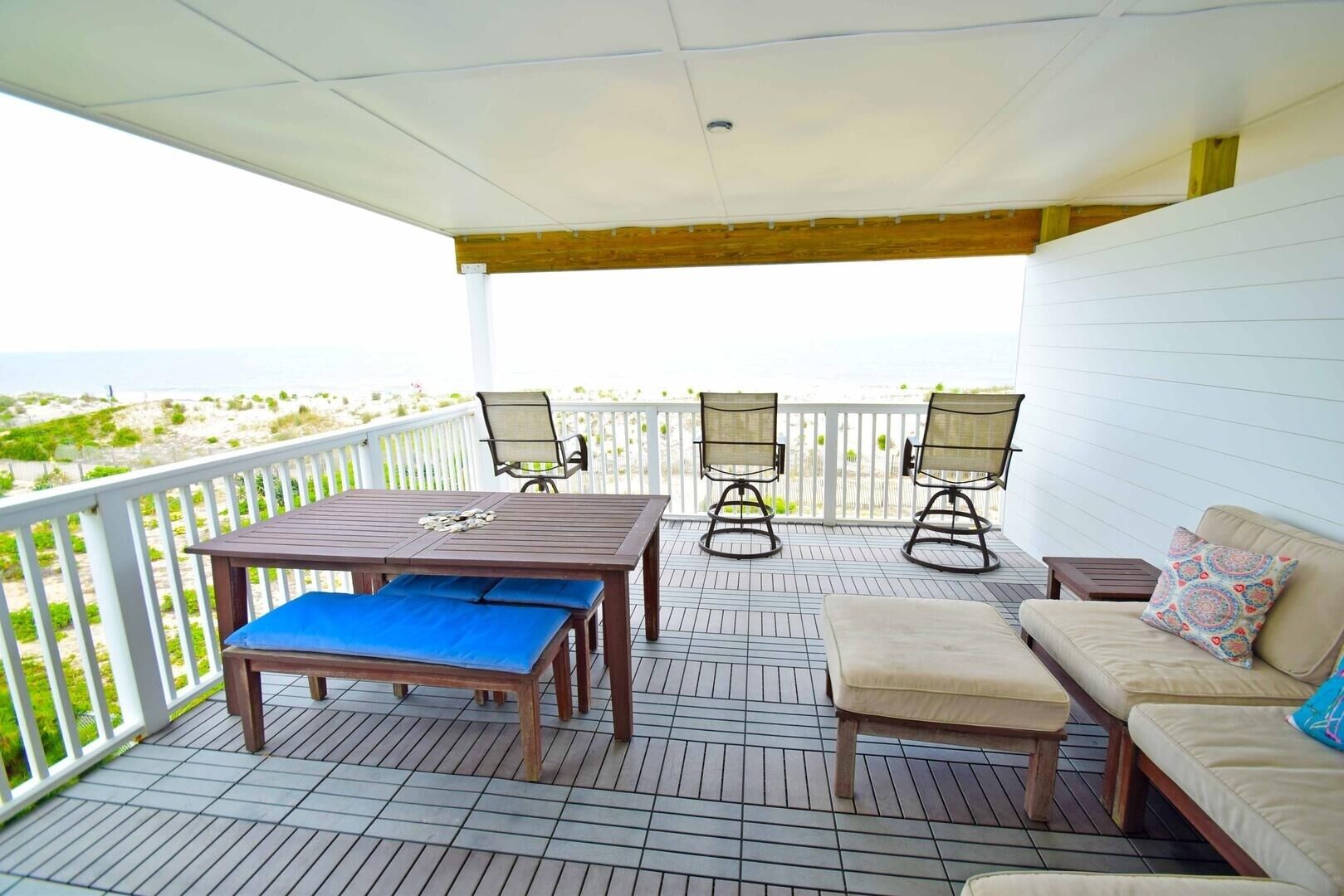 Een overdekt terras buiten met een houten tafel, twee stoelen, een bank en een lange zitbank.