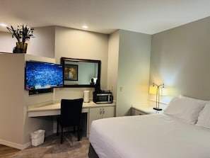 Ein Hotelzimmer mit Bett, Schreibtisch, Stuhl, Fernseher, Mikrowelle und Lampe.