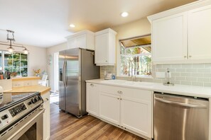 A modern kitchen with white cabinets, stainless steel appliances, and a wooden countertop. - Stella 3 Bedroom Home (Bend)