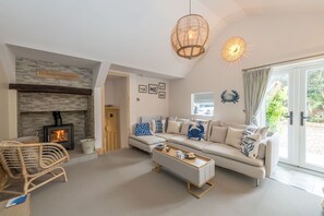Una sala de estar con chimenea, sofá, mesa de centro, sillón de mimbre y un amplio ventanal.