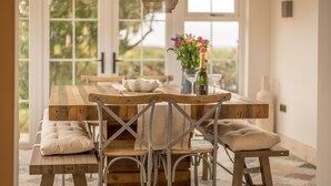 Una mesa de comedor de madera con sillas de metal y bancos acolchados, un florero con flores y una lámpara colgante.