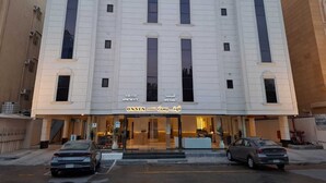 A multi-story building with a central entrance, large windows, and a sign indicating serviced apartments. - Onsen Hotel Al Shati (Dammam)