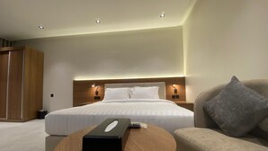 A modern hotel room with a large bed, bedside lamps, a round wooden table, and a sofa. - Onsen Hotel Al Shati (Dammam)