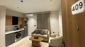 A modern apartment with a kitchenette, a sofa, a coffee table, and a door marked with the number 409. - Onsen Hotel Al Shati (Dammam)