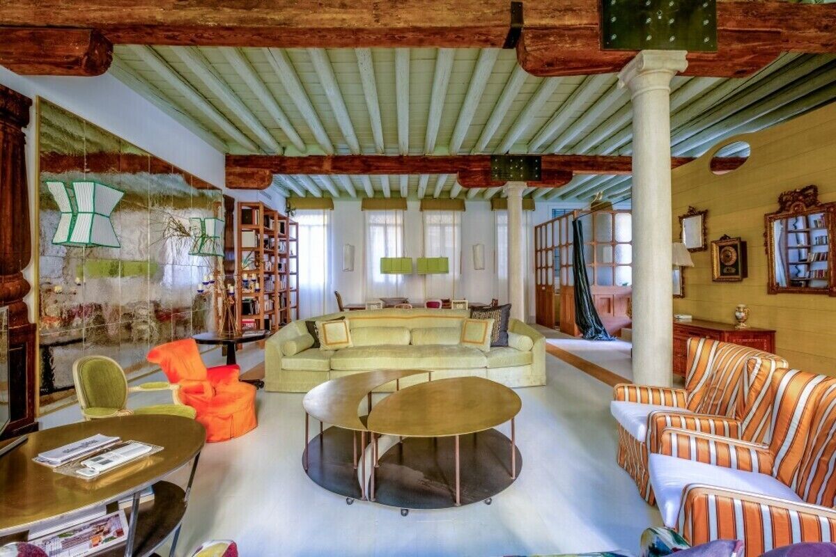 A spacious living room with a large sofa, a coffee table, and a striped armchair. There are bookshelves and a fireplace.