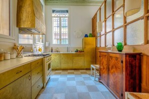 Une cuisine avec un carrelage à motifs, des placards en bois, une fenêtre et un petit tabouret.
