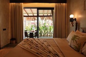 Quarto de hotel com cama, cortinas, mesa e cadeiras, e vista para um jardim.