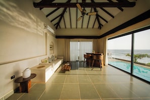 Ampla sala de estar com uma grande janela com vista para uma piscina, ventoinha no teto e área de jantar.