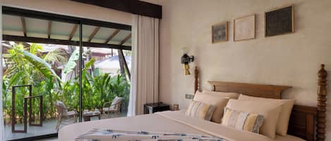 A hotel room with a large bed, a nightstand, a lamp, and a view of a tropical garden.