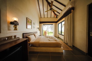 A bedroom with a bed, a desk, a ceiling fan, and a large window with curtains.
