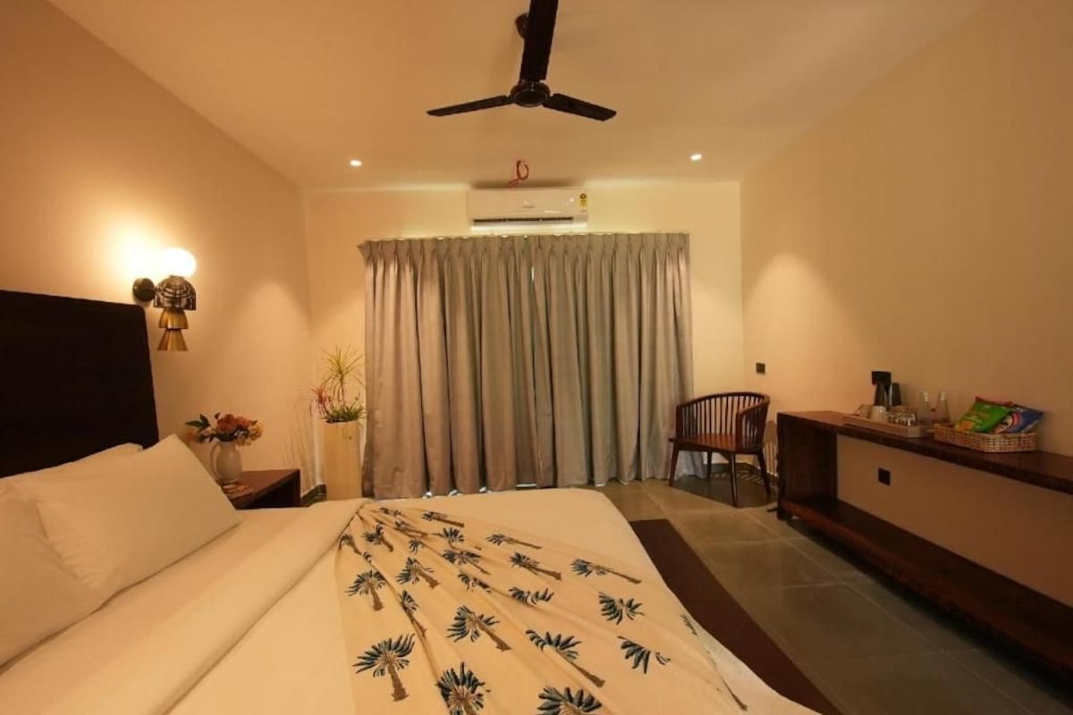 A hotel room with a bed, a desk, a chair, a ceiling fan, and a window with curtains.