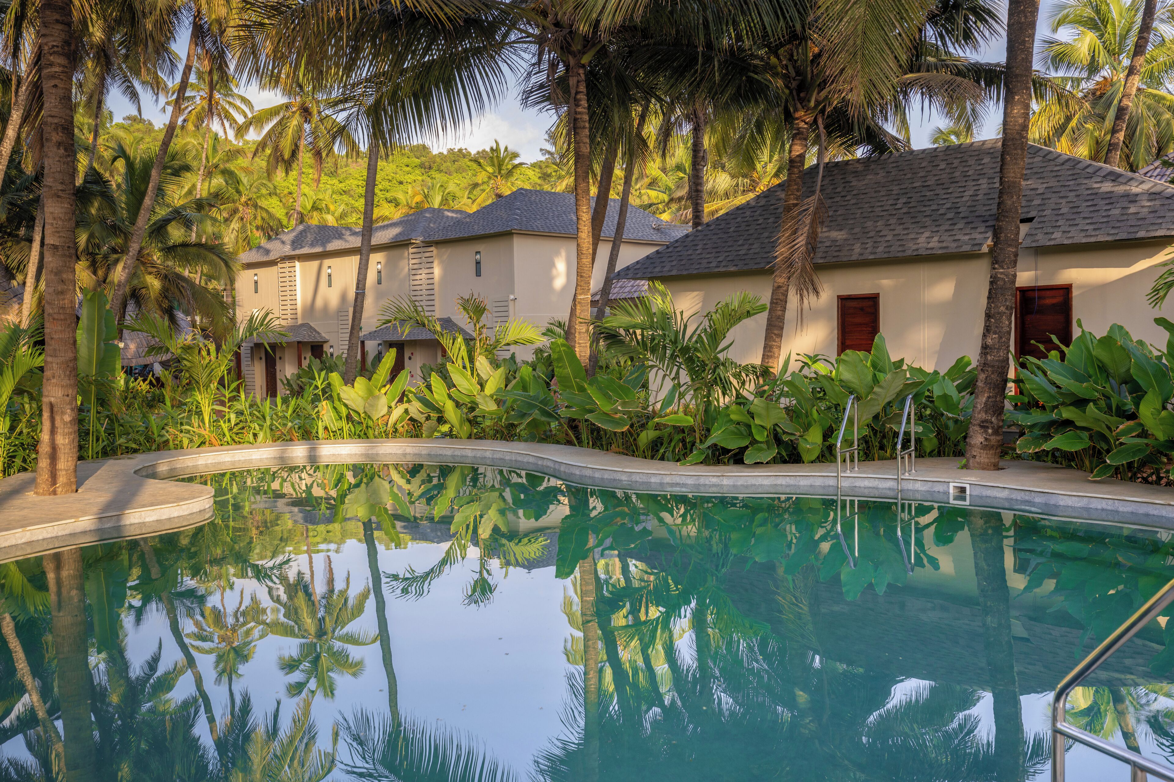 A swimming pool surrounded by palm trees and a building with a tiled roof.