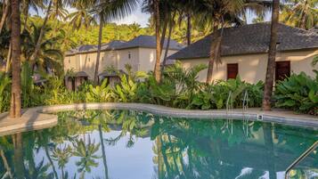 A swimming pool surrounded by palm trees and a building with a tiled roof.