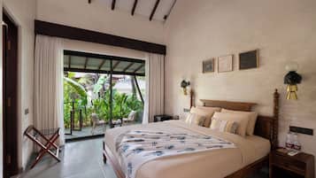 A bedroom with a large bed, a nightstand, a lamp, and a view of a tropical garden through a sliding door.