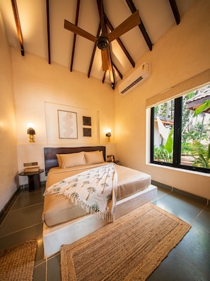 Quarto com cama, janela com vista, ventilador de teto e ar condicionado fixado na parede.