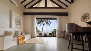 A spacious living room with a view of the ocean, a piano, and a dining area. - The Earth-Maison Ocean Beach Resort (Ashvem)